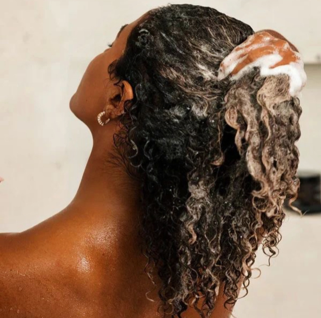 Женщина использует лучший шампунь для увеличения объема для женщин с тонкими волосами в душе, уделяя особое внимание уходу за кожей головы