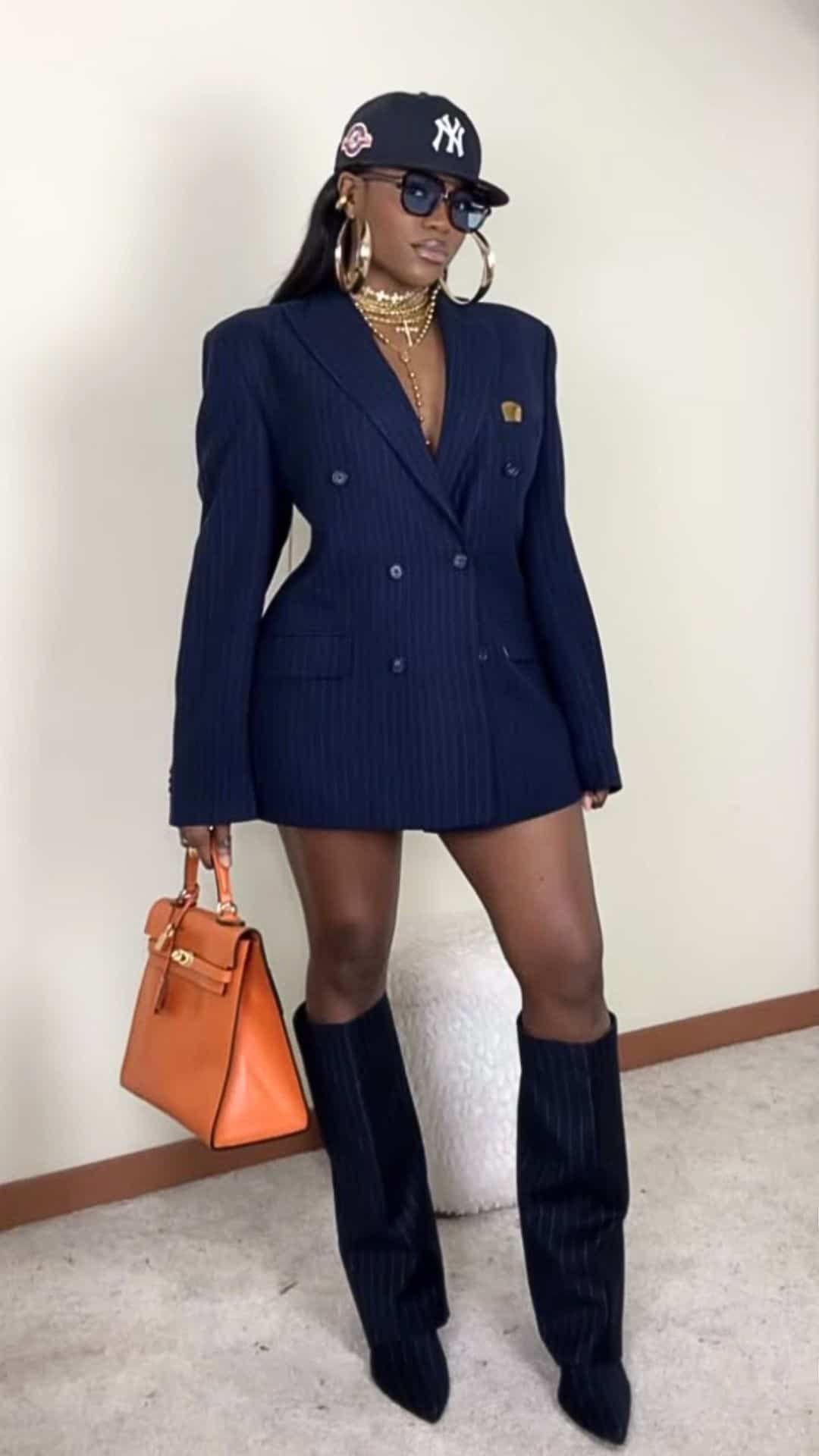 миниатюрная женщина в мини-платье-блейзере с украшениями, кепке и оранжевой сумке