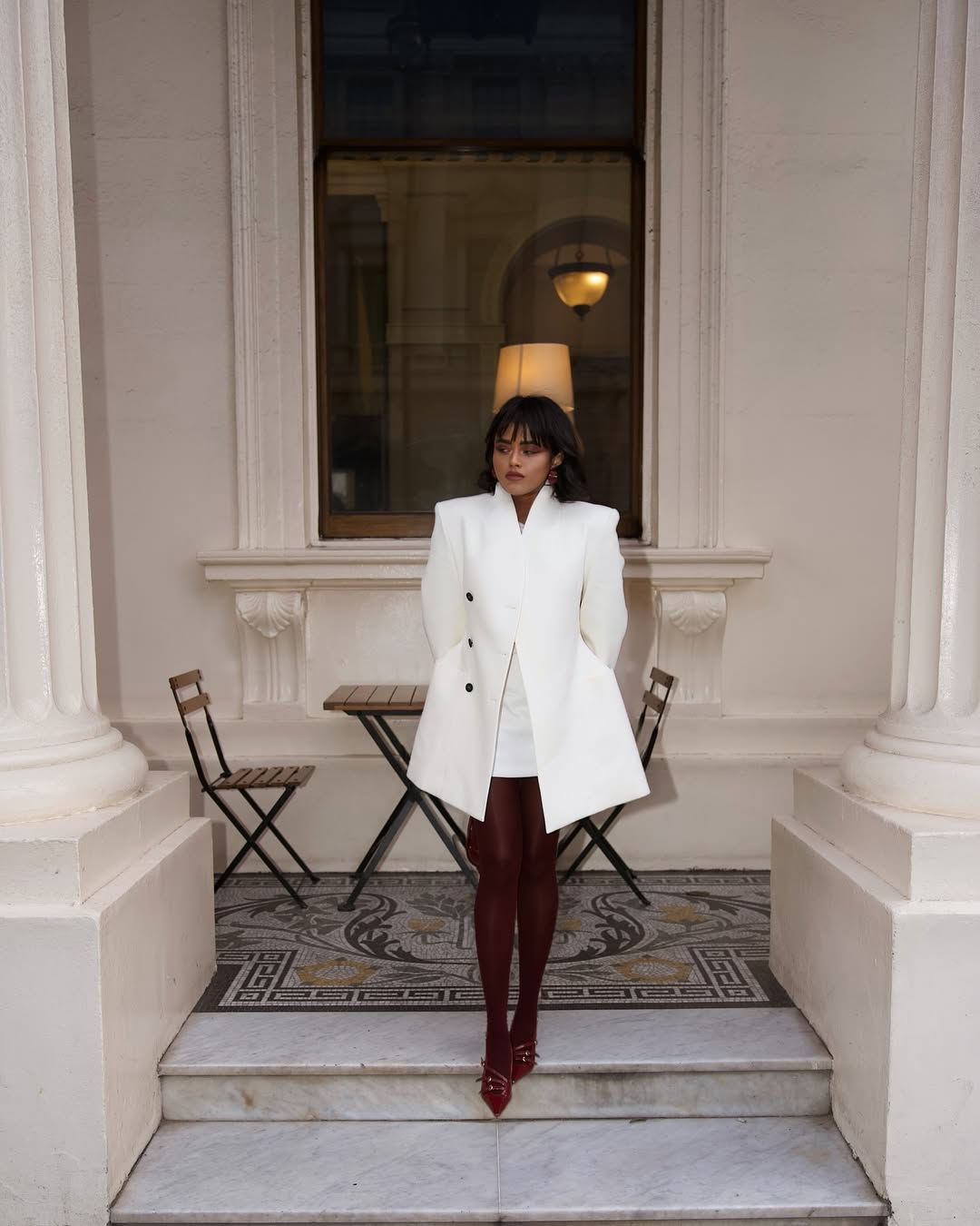 Model wearing burgundy tights outfit with a white mini skirt and long winter coat.