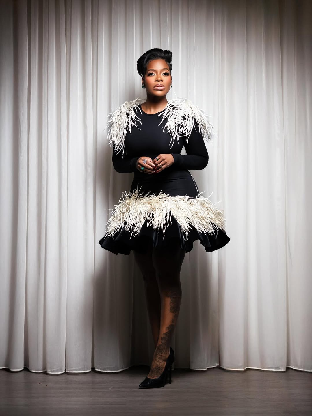 Fantasia attends the RockSoul & Salute Company Christmas Party wearing a black feather-trimmed Christian Siriano dress