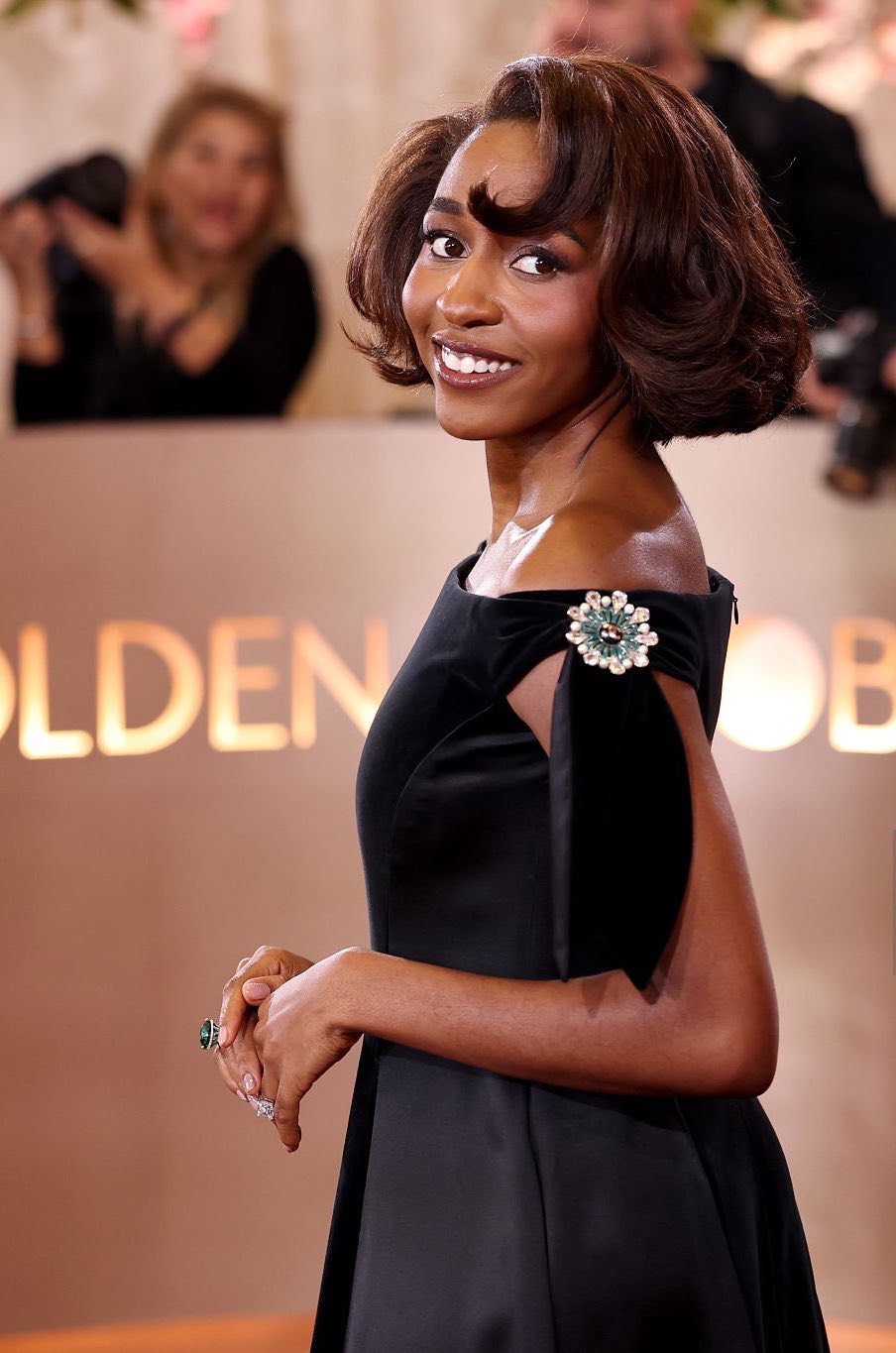Ayo Edebiri wearing a voluminous red-tinted bob hairstyle with soft curls and side-swept bangs on the 2026 Golden Globes red carpet