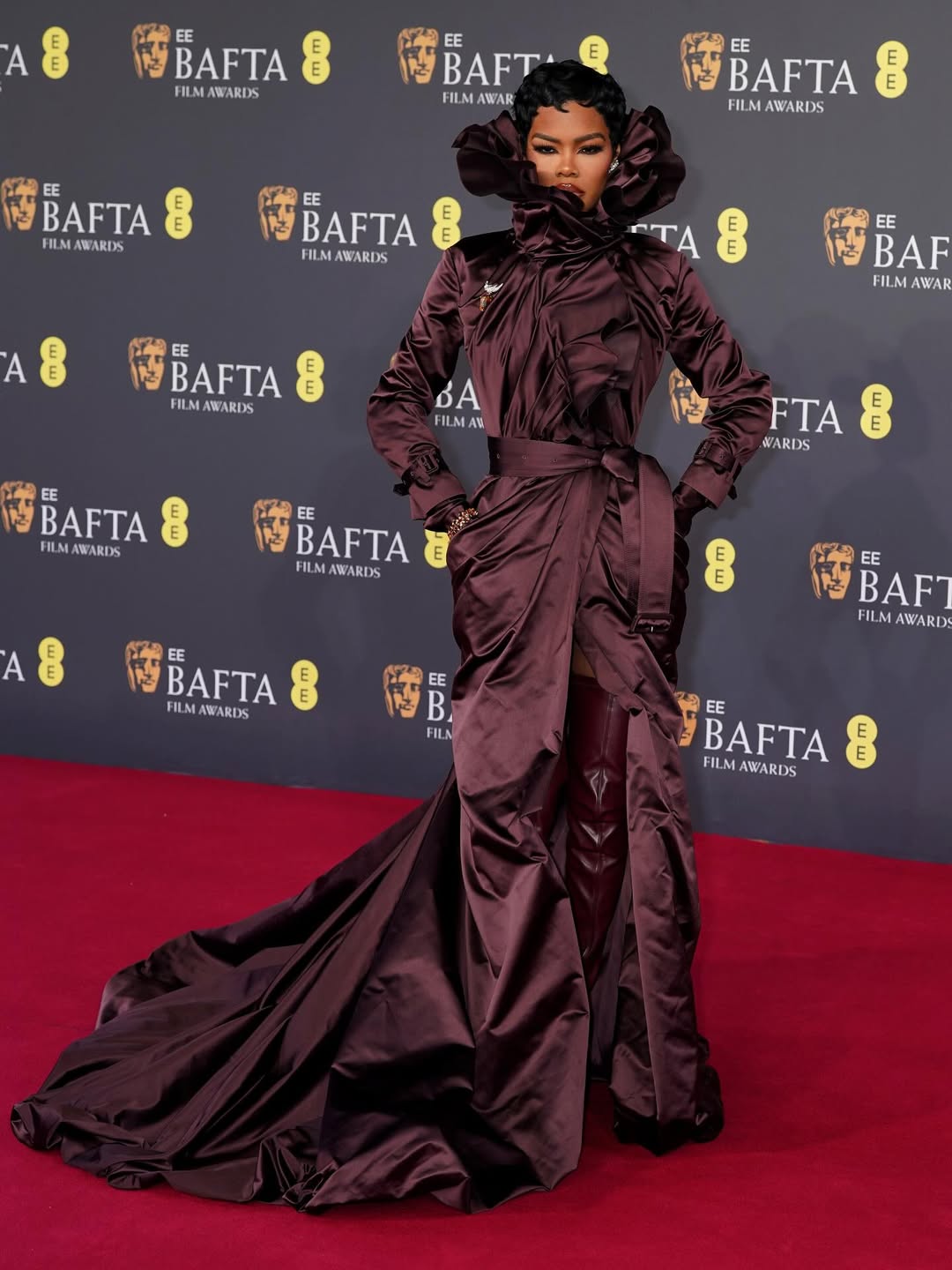 Teyana Taylor at the BAFTAs in dramatic oxblood satin ensemble with cinched waist, cascading ruffles, and sweeping train.