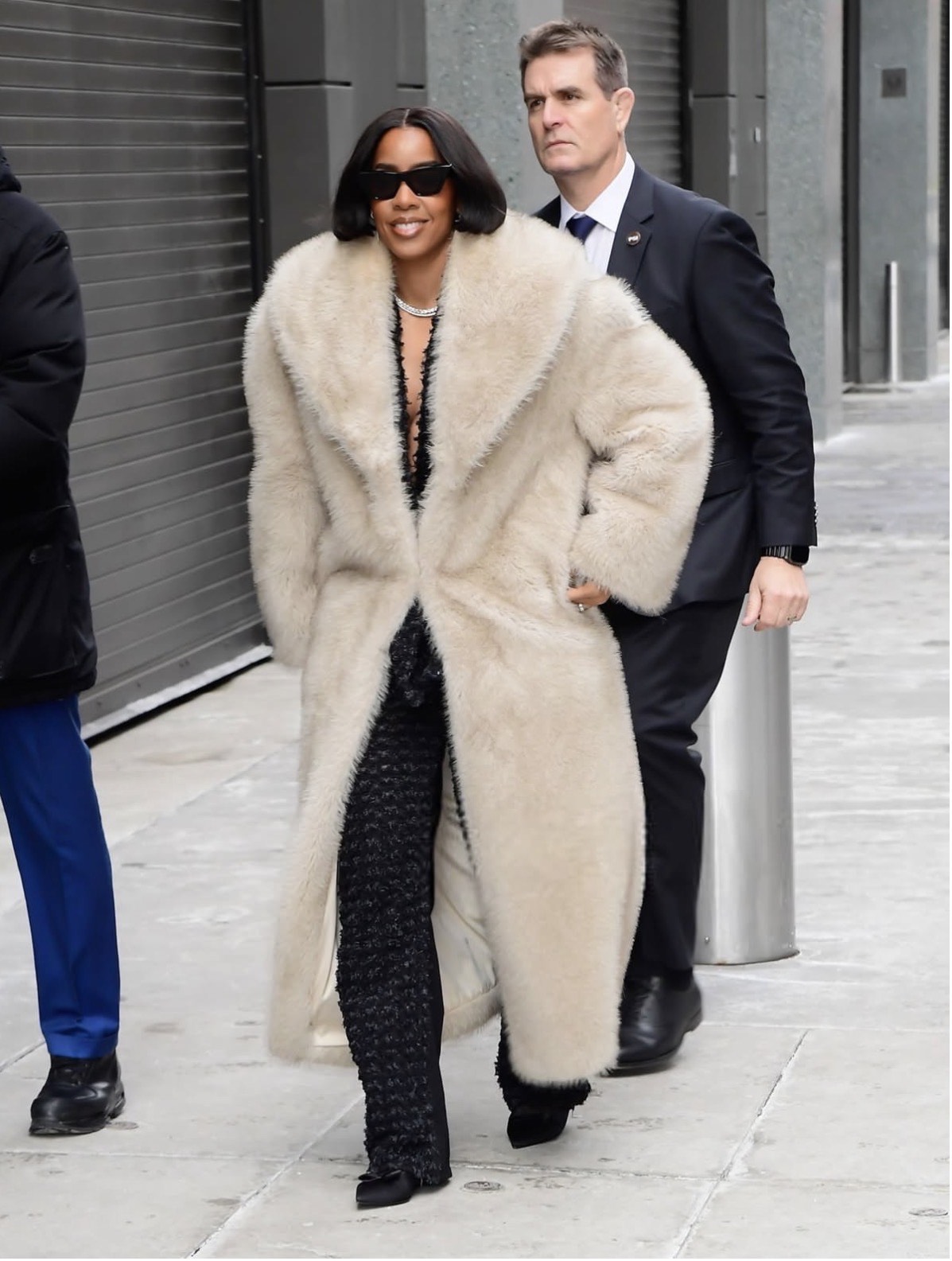 Kelly Rowland in a cream faux-fur coat layered over a plunging black top and textured wide-leg pants with layered necklaces and dark sunglasses — Valentines party outfit ideas