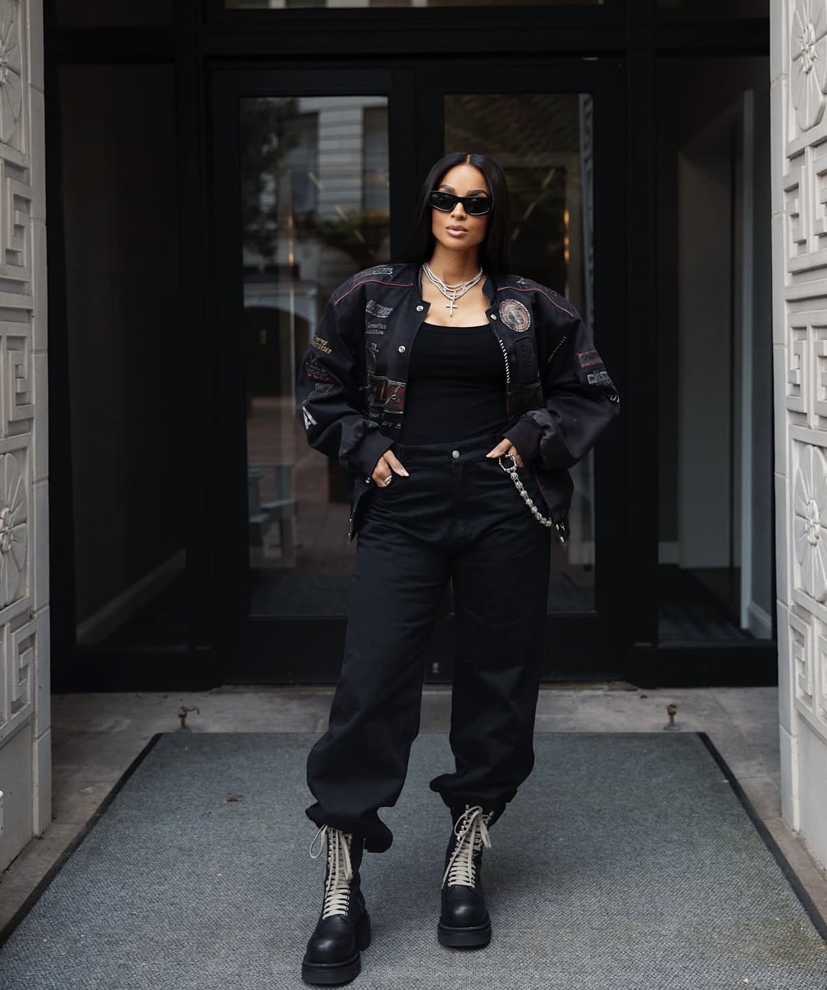 Ciara in a graphic varsity jacket, cargo pants, and combat boots styled with layered silver jewelry and statement sunglasses for an edgy streetwear look.