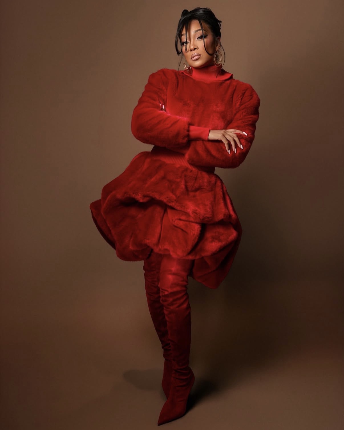 Monica Denise is wearing a red textured bubble-hem dress with thigh-high suede boots in a bold monochromatic ensemble.