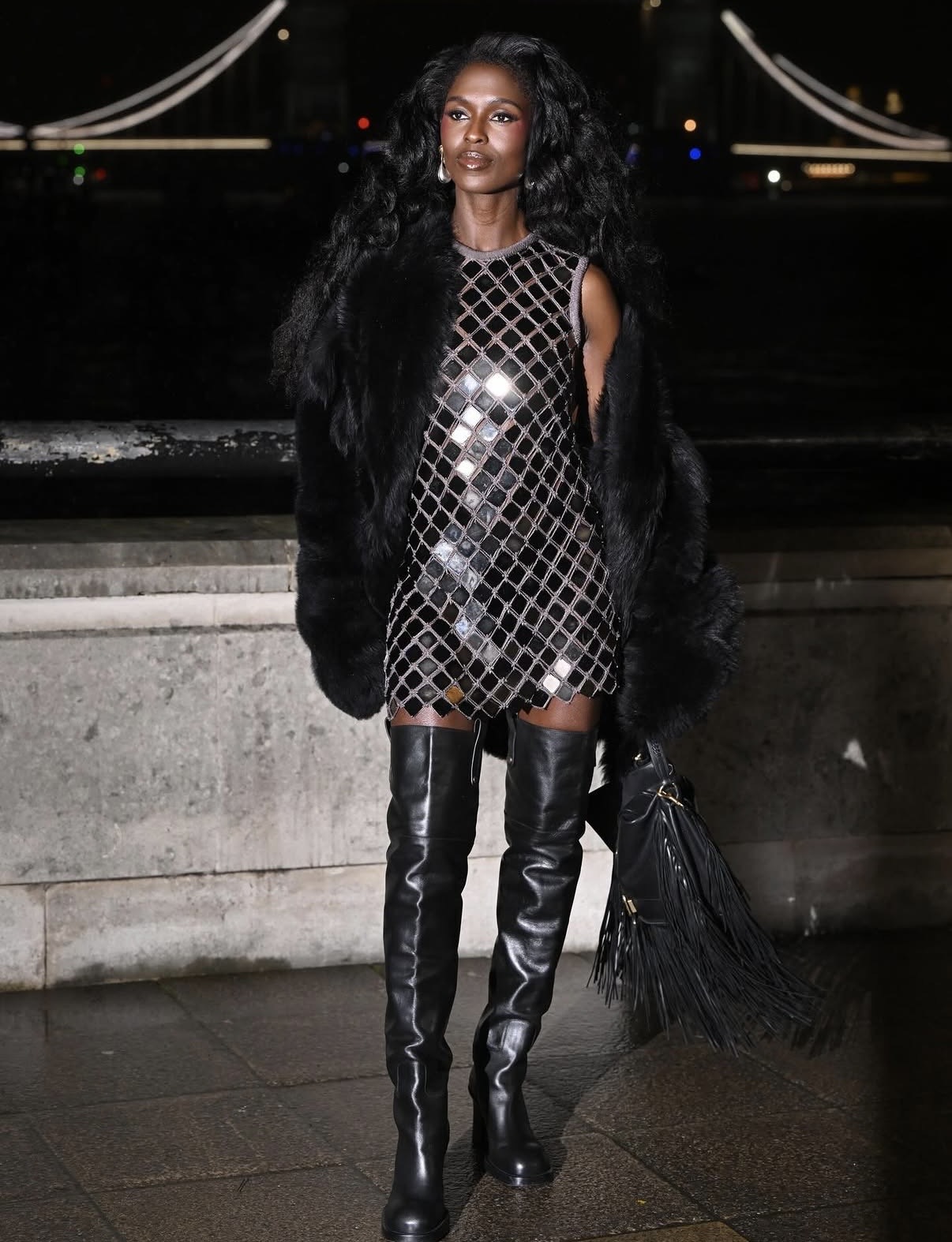 Jodie Turner-Smith in a mirrored sequin micro mini dress layered with a black fur coat and thigh-high boots at London Fashion Week — late-winter celebrity outfits