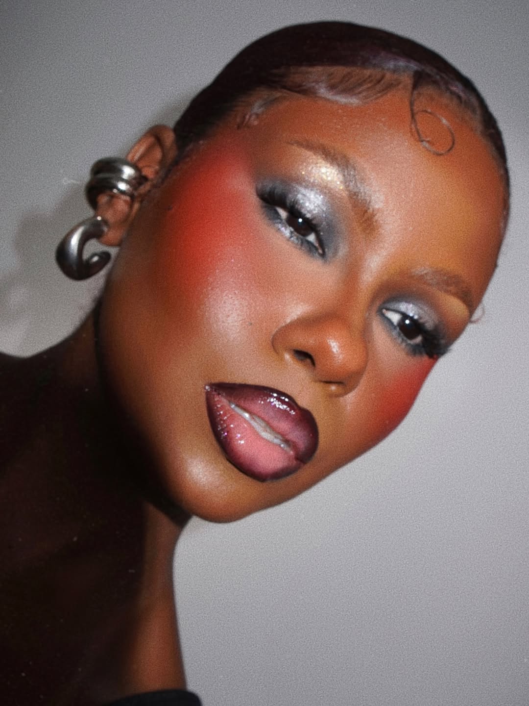 black woman wearing silver eyeshadow with stick blush and glossy lips