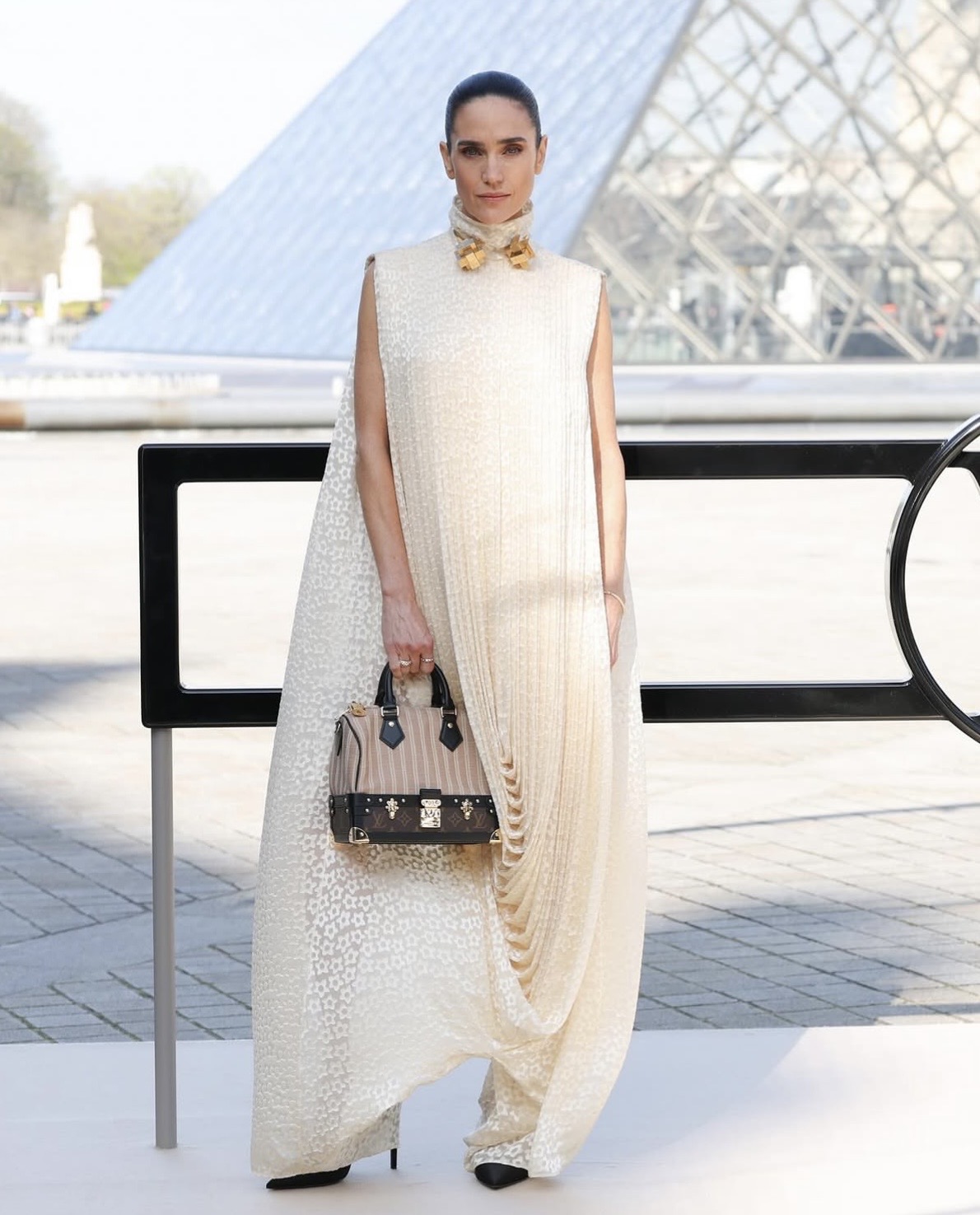 Jennifer Connelly in a cream pleated Louis Vuitton draped jumpsuit with gold collar hardware at the Paris runway show.