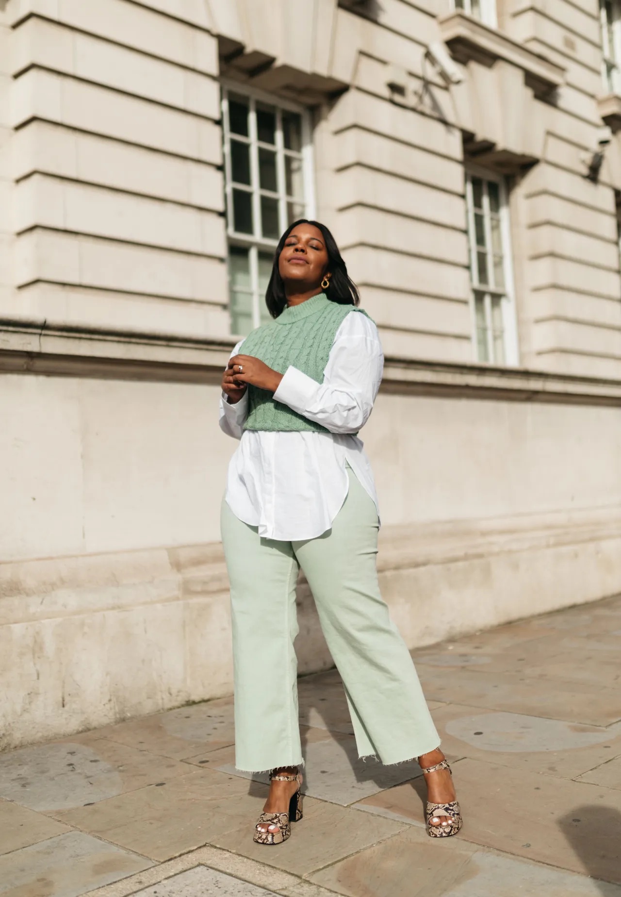 A sage knit vest layered over a white shirt with trousers for office styling— sage green styling for spring